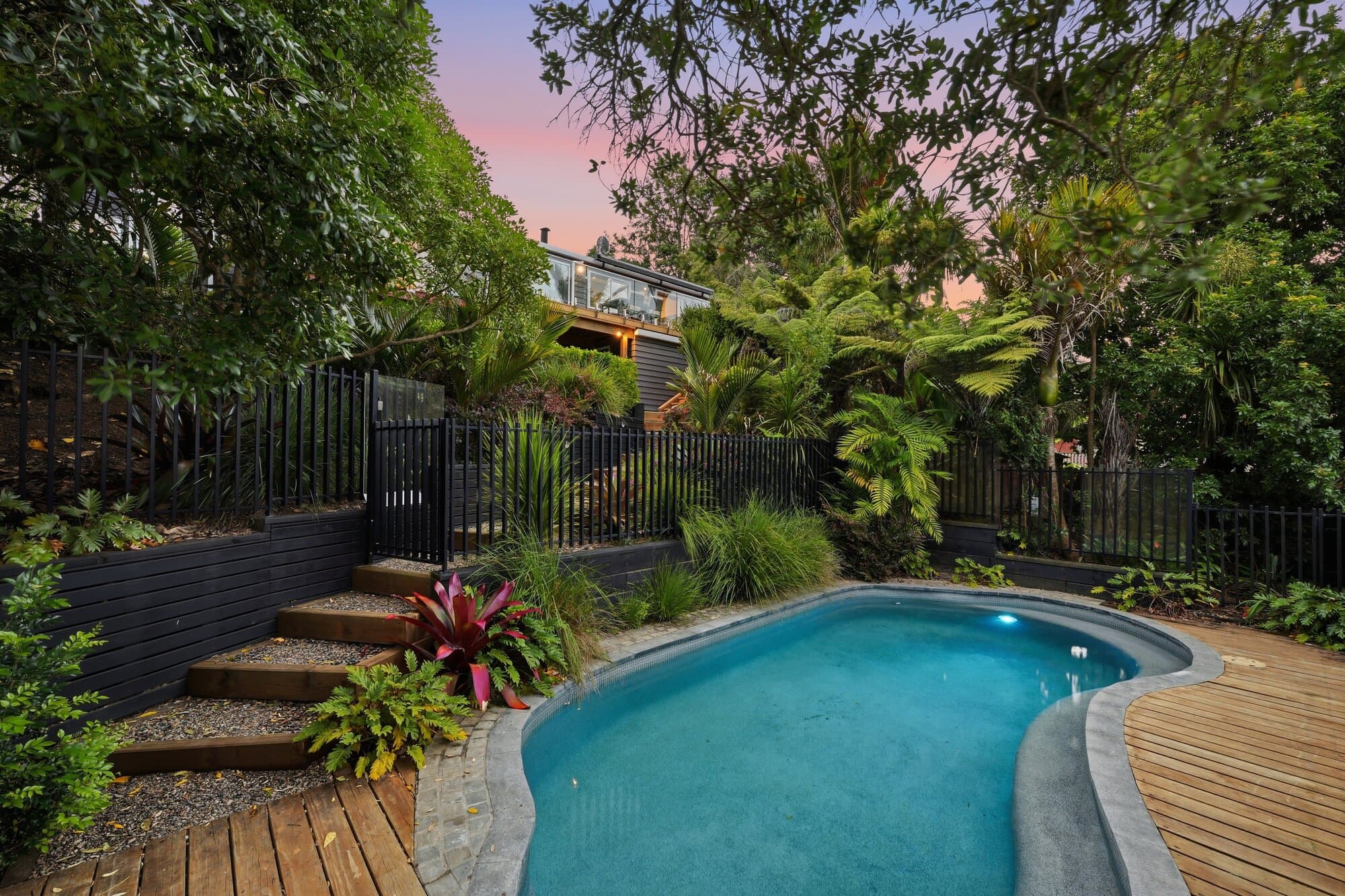 Pool and deck at twilight surrounded by tropical landscaping